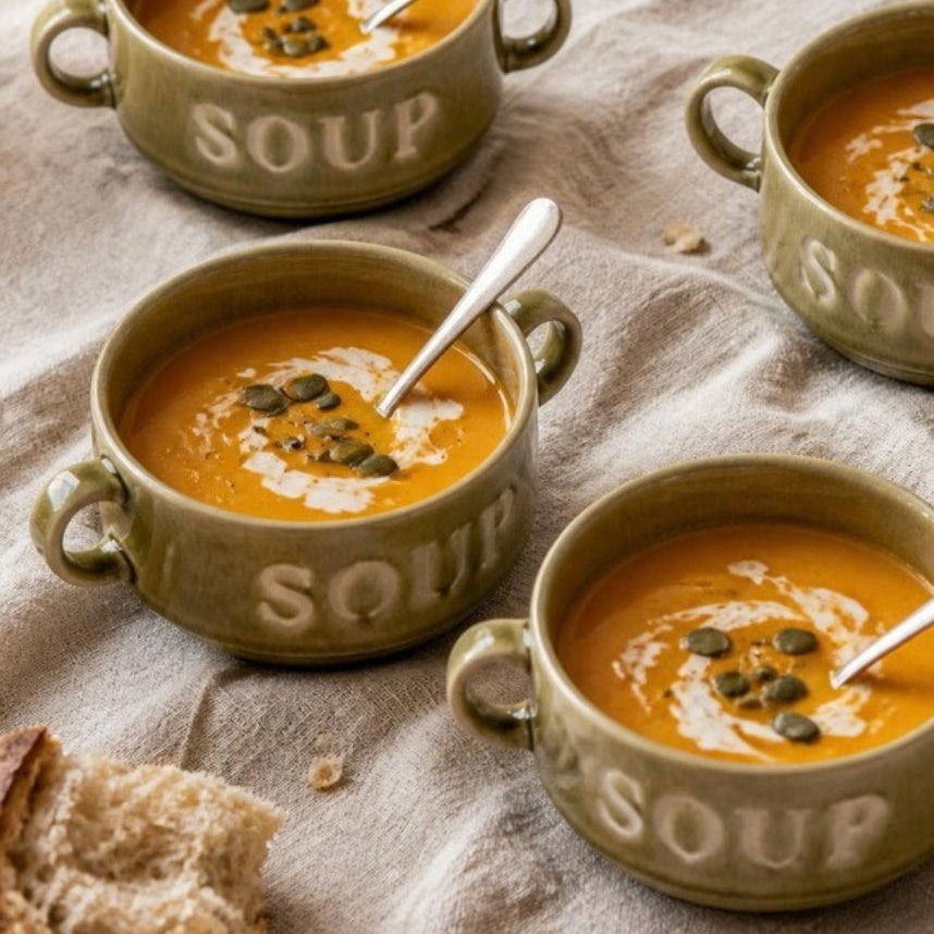 Vier groene Soup soepkommen met pompoensoep op een gedekte tafel, van bovenaf